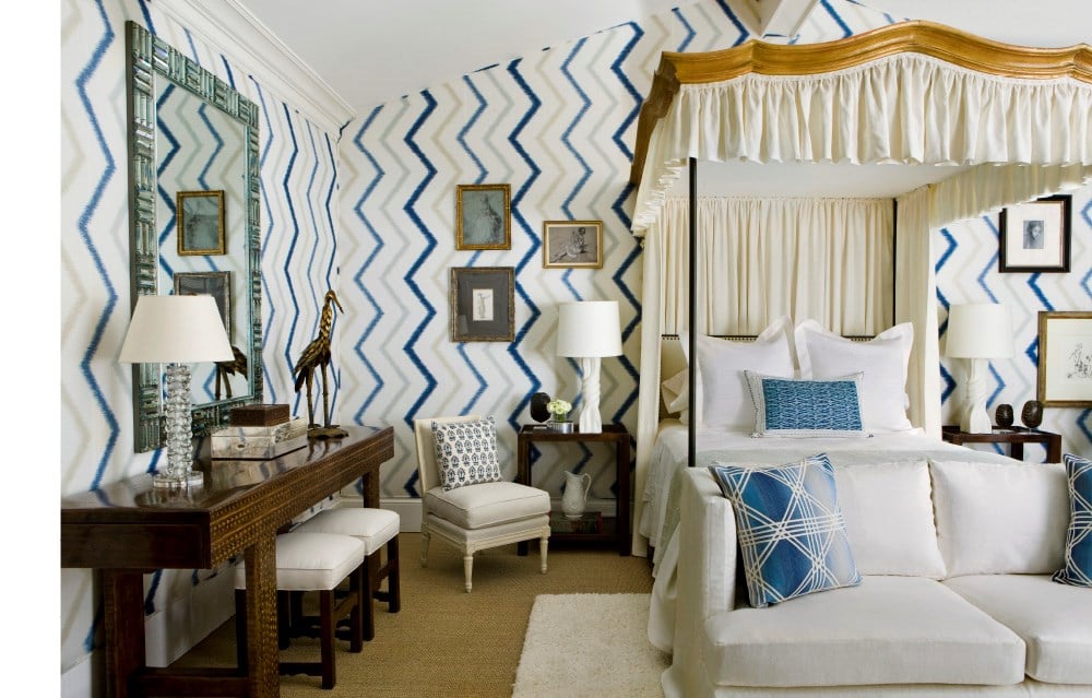 A bedroom adorned with zigzag patterned walls, a white canopy bed, and blue decorative pillows offers an evocative setting. A wooden desk is complemented by white stools and a chair featuring a matching zigzag pillow, embodying the luxurious home interiors depicted in Common Ground's "Atmosphere: The Seven Elements of Great Design.