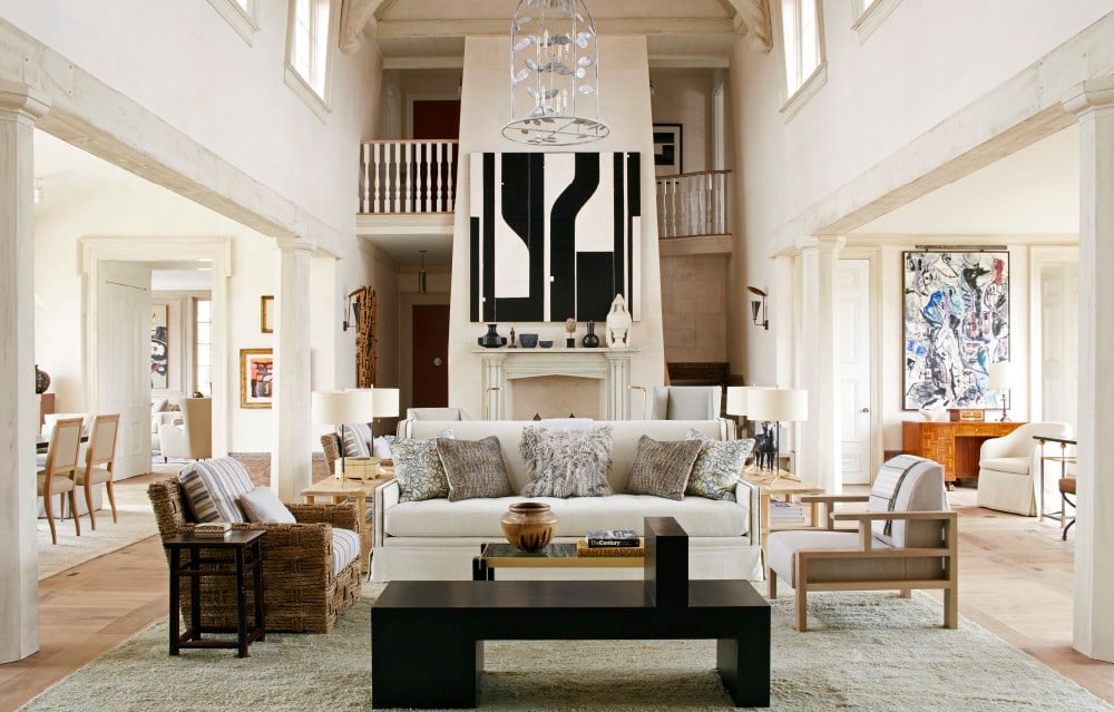 A contemporary living room with high ceilings, white walls, modern furniture, evocative artwork on the walls, and a large fireplace as the focal point embodies the principles of "Atmosphere: The Seven Elements of Great Design" by Common Ground.