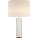 A Lineham Table Lamp by Visual Comfort with a cylindrical clear glass body, antique brass accents, and a large, round, beige lampshade.