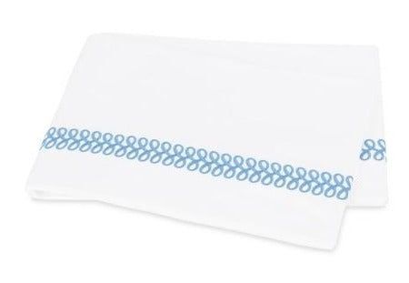 White towel with a decorative blue Matouk Astor Braid pattern along one edge, displayed on a plain background.