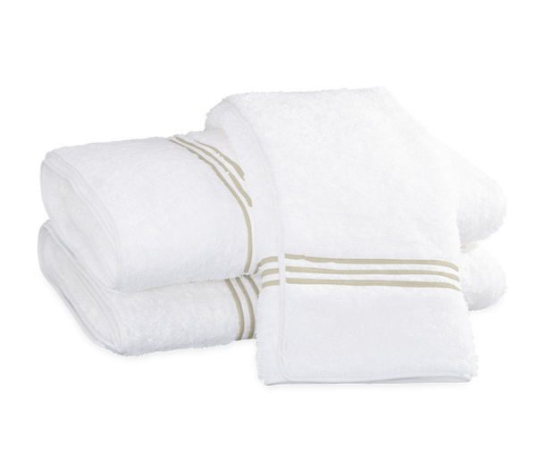 A stack of Matouk Bel Tempo Bath Collection - Almond towels, with decorative beige stripes, neatly folded on a black background.