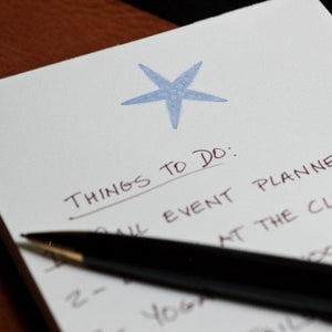 A close-up of a pen on a Printery Starfish Notepad in Bone White, featuring "Things To Do:" at the top and a blue starfish above the text.
