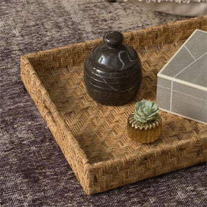 The Cadie Natural Flat Small Rattan Tray by Made Goods artfully showcases a decorative jar, a small plant in a textured pot, and a box on a chevron-patterned fabric surface.