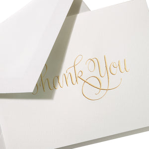 The Crane Gold Thank You Card Set features white cotton paper cards with "Thank You" in gold calligraphy, each partially tucked into a matching white envelope.