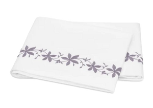 A folded white bed sheet from the Matouk Callista Bedding Collection, Lilac, features lilac floral embroidery along one edge and is crafted from luxurious Giza Egyptian cotton.