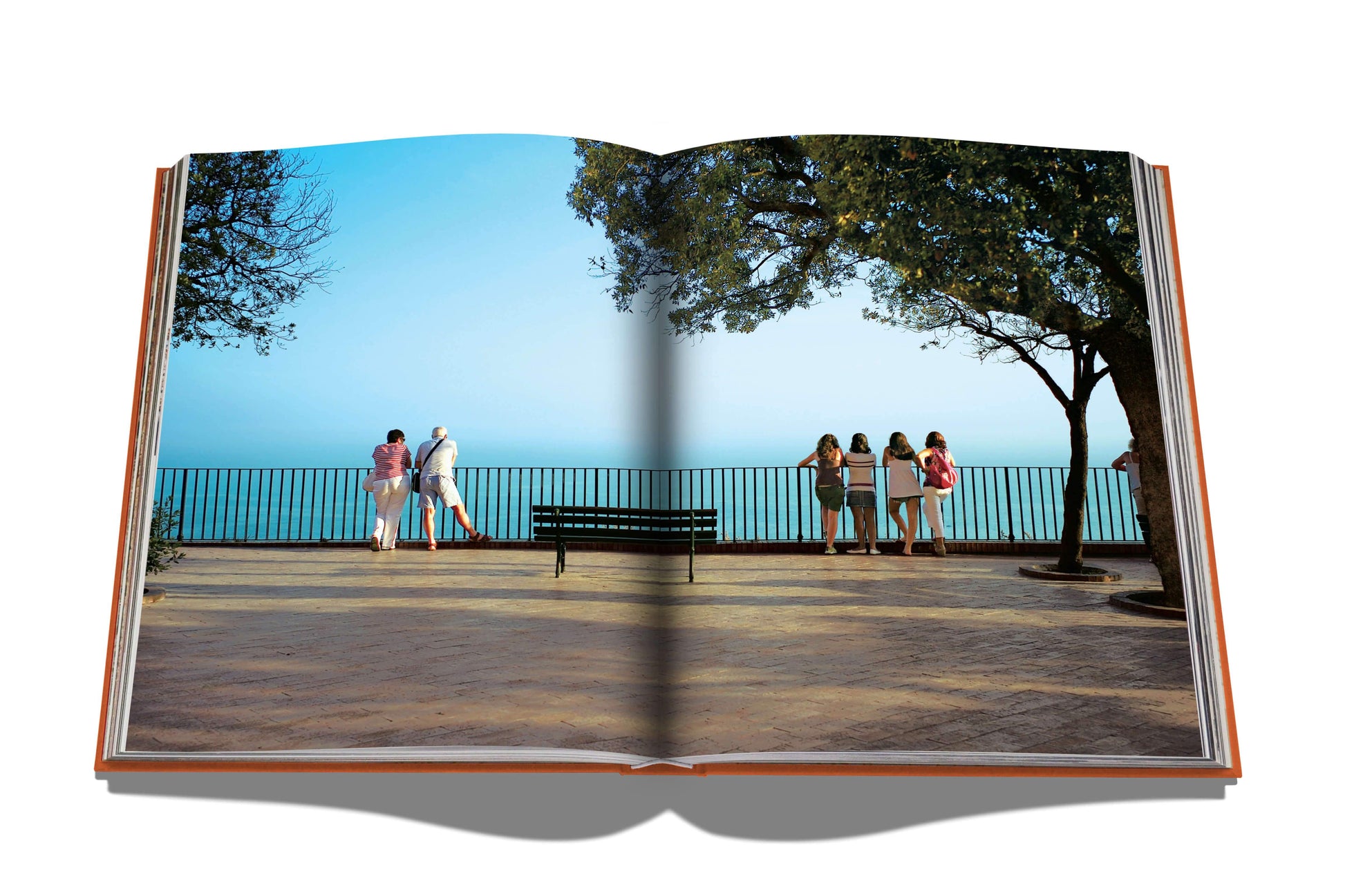 An Assouline book displaying a photograph of people gathering and chatting by a railing overlooking a body of water, embodying the Mediterranean spirit, with a shadow of Capri Dolce Vita's spine dividing the image.