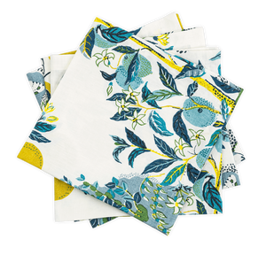 The Matouk Citrus Garden Pool Napkin Set features folded napkins with blue and green floral patterns on a white background, accented with yellow, adding Josef Frank's artistic touch to your table setting.