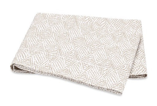 Folded beige Matouk Duma Diamond bedding fabric on a white background. 