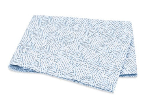 A folded blue and white Duma Diamond Bedding Collection towel by Matouk, featuring a geometric pattern, is displayed on a white background.