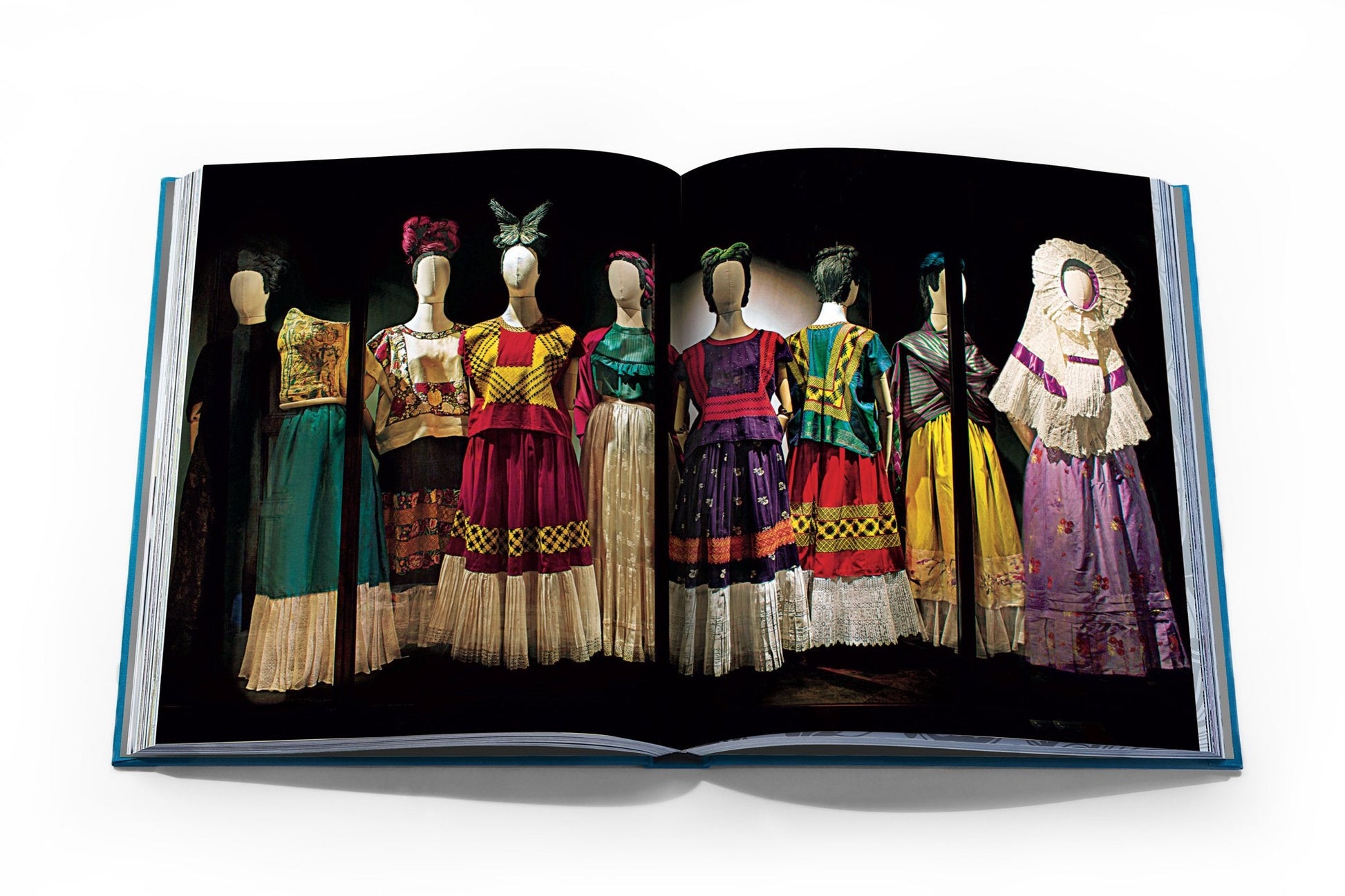 The book, "Frida Kahlo: Fashion As the Art of Being" by Assouline, showcases mannequins adorned in traditional Mexican attire with colorful embroidery and patterns, capturing the timeless style reminiscent of iconic artist Frida Kahlo.