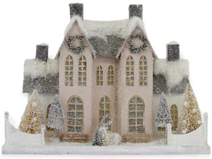 The Cody Foster Elegant Ivory Manor is a miniature paper mache model of a large, light house with a snowy roof, wreaths, trees, and a white fence that evokes a charming winter or holiday scene.