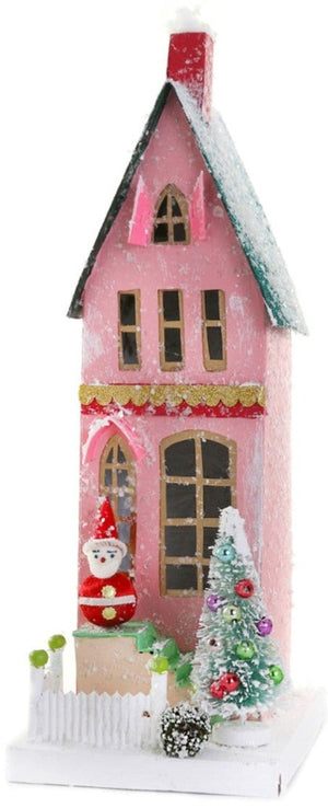The Cody Foster Vintage Santa Townhome is a pink, handcrafted model house with snow accents, a Santa figurine, decorated Christmas tree, white picket fence, and a small front wreath.