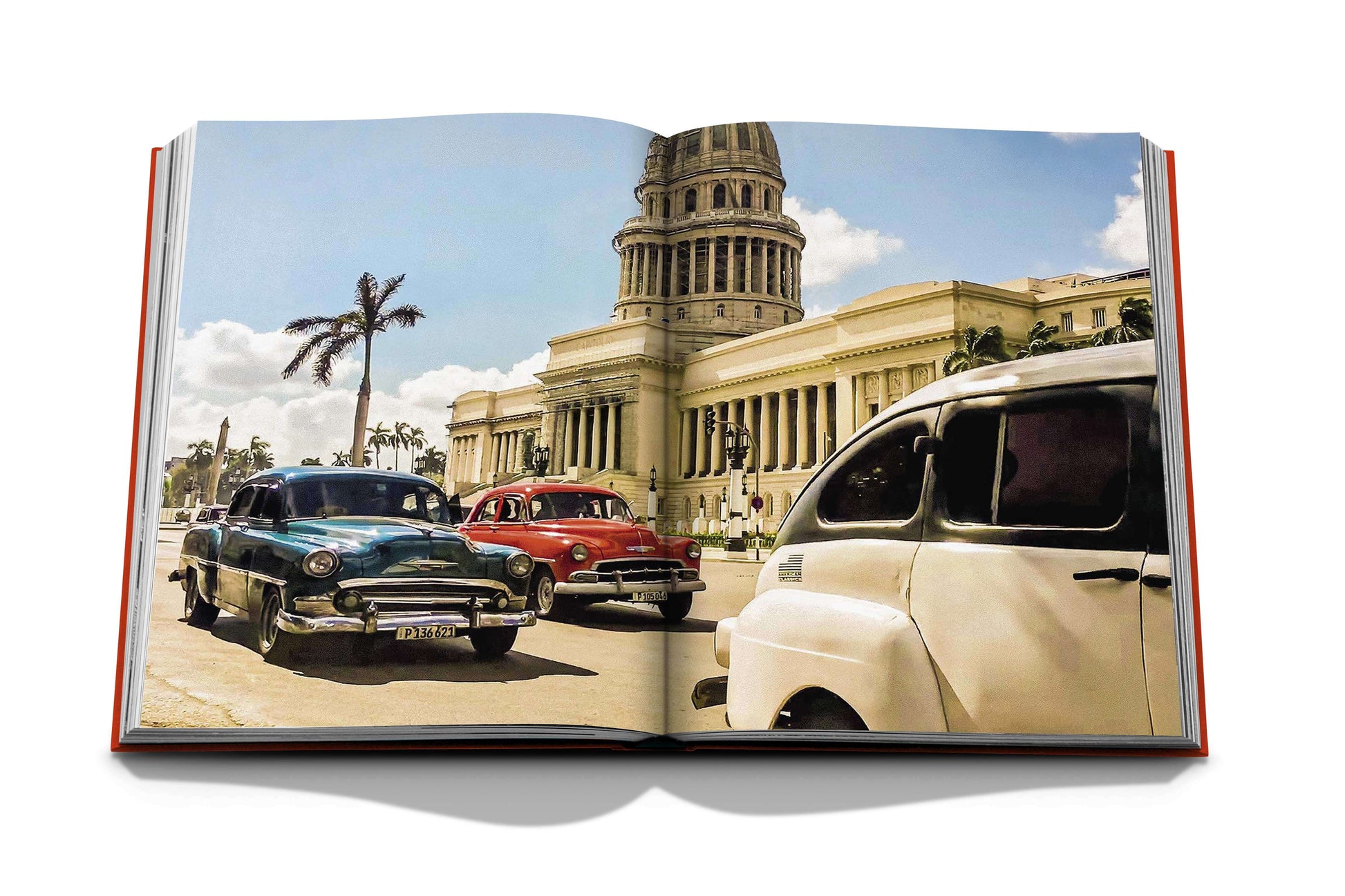 A book opened to a page showing a vintage photograph of classic cars driving in front of an ornate building with palm trees, resembling a historic cityscape during Havana's cultural renaissance, from the Assouline collection titled "Havana Blues.