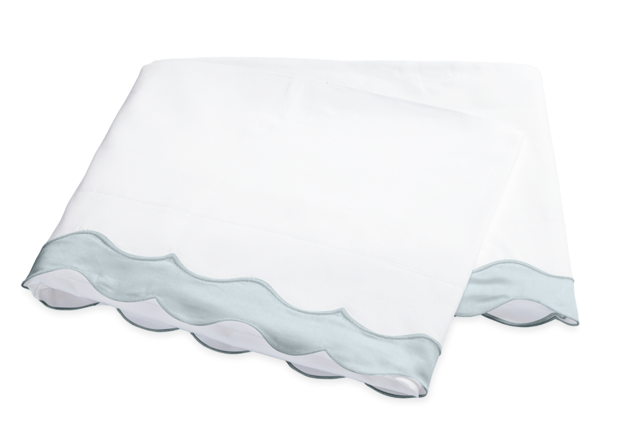 A folded white bedsheet from the Matouk Lorelei Bedding Collection in Pool, featuring a light blue 600 thread count percale scallop applique trim, displayed on a plain background.