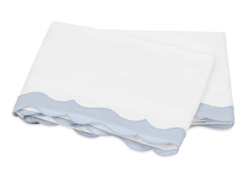 White and blue Matouk Lorelei Bedding Collection baby blanket with a scalloped edge, crafted from Milano Egyptian cotton, folded on a white background.
