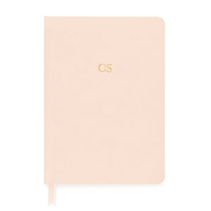 The Sugar Paper Tailored Pale Pink Journal is a closed hardcover with gold "CS" initials, a matching grosgrain ribbon bookmark, and lined pages for organized notes.