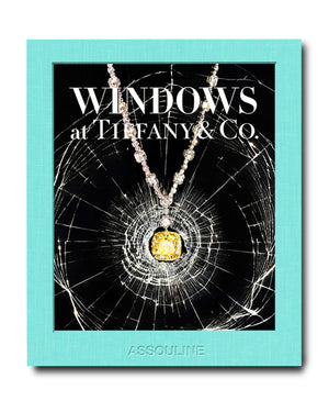 The book cover, "Windows at Tiffany and Co." by Assouline, features a backdrop of shattered glass and highlights a yellow gemstone necklace, evoking Gene Moore's iconic Tiffany & Co. window displays.
