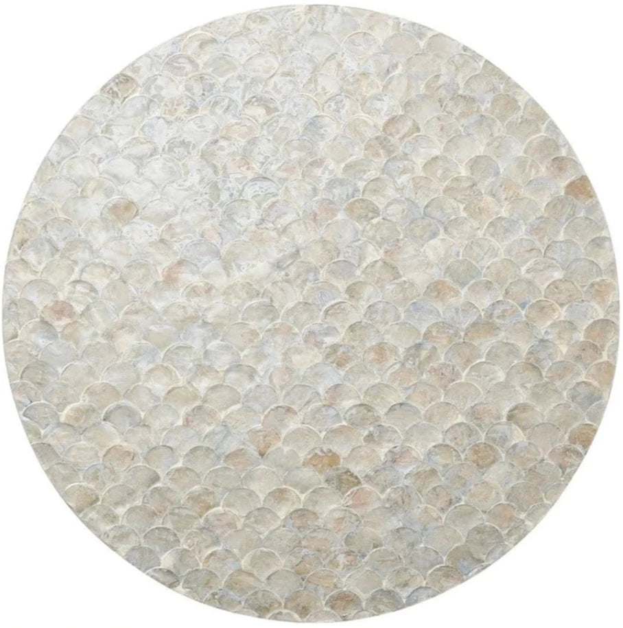 The Camellia Gray Placemat by Kim Seybert features a scalloped round design, crafted from hand-dyed Capiz shells arranged in an iridescent mosaic pattern reminiscent of delicate fish scales.