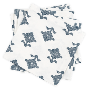 A stack of Matouk's Rubia Navy Napkin Set, featuring white OEKO-TEX® Standard 100 certified napkins with a blue floral pattern, is arranged slightly askew on a black background.