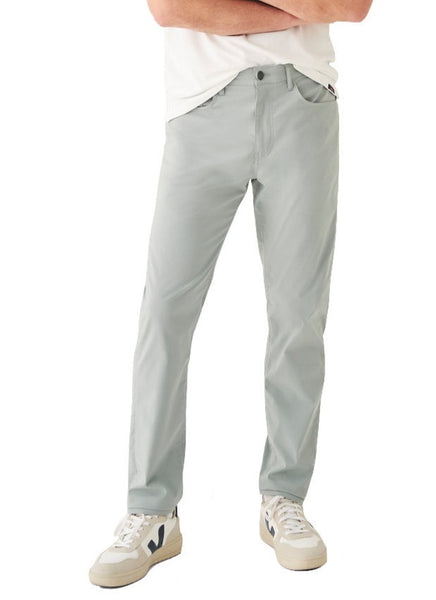 A person standing with arms crossed wearing light grey Faherty Movement Five Pocket Pants with COOLMAX® CORE Technology and white sneakers for enhanced comfort.