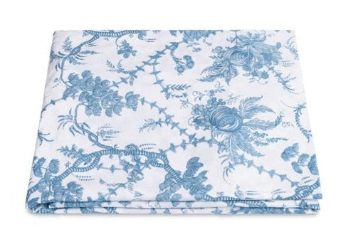 A folded white fabric featuring a blue floral and vine pattern from the San Cristobal Bedding Collection, Sky by Matouk, crafted from luxurious Luca Egyptian cotton percale.