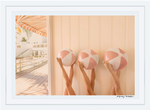 Three pairs of arms holding Gray Malin The Cabana beach balls against a wooden wall with a Palm Beach poolside setting in the background.