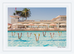Eight synchronized swimmers with raised legs create a classic Gray Malin vibe, set before a mid-century building and palm trees in "Gray Malin Pool Party, White Frame, 29.5\" x 41.5\"" by Gray Malin—a true poolside scene.