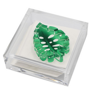 The Tara Wilson Designs Lucite Cocktail Napkin Holder with Monstera Leaf Weight includes white napkins and a decorative green acrylic monstera leaf, making it a stylish and fun hostess gift.