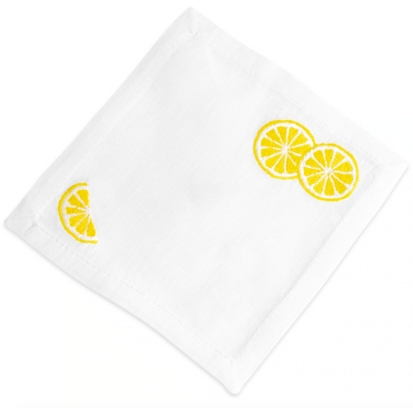 White linen cloth napkin with three hand-embroidered yellow lemon slices in one corner, displayed on a plain white background for the Lemon Slice Coasters by Haute Home.