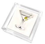 The Tara Wilson Designs Lucite Cocktail Napkin Holder with Martini Weight features a silver martini glass pin with an olive detail, displayed on a white background inside a clear acrylic holder.