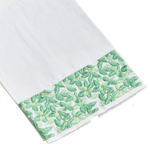 A Haute Home Boxwood Tip Towel, a white linen cloth with a decorative green floral pattern along one edge, isolated on a black background.