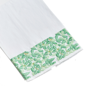 A Haute Home Boxwood Tip Towel, a white linen cloth with a decorative green floral pattern along one edge, isolated on a black background.