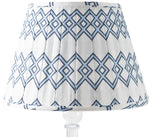 The Lattice Shade in Blue by Sorella Glenn features a geometric blue diamond pattern and box pleat detail, shown on a clear base—perfect for adding a classic preppy touch to any room.