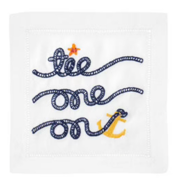 A white August Morgan linen napkin with the embroidered phrase "tie one on" in blue cursive, accented with small yellow and orange details.