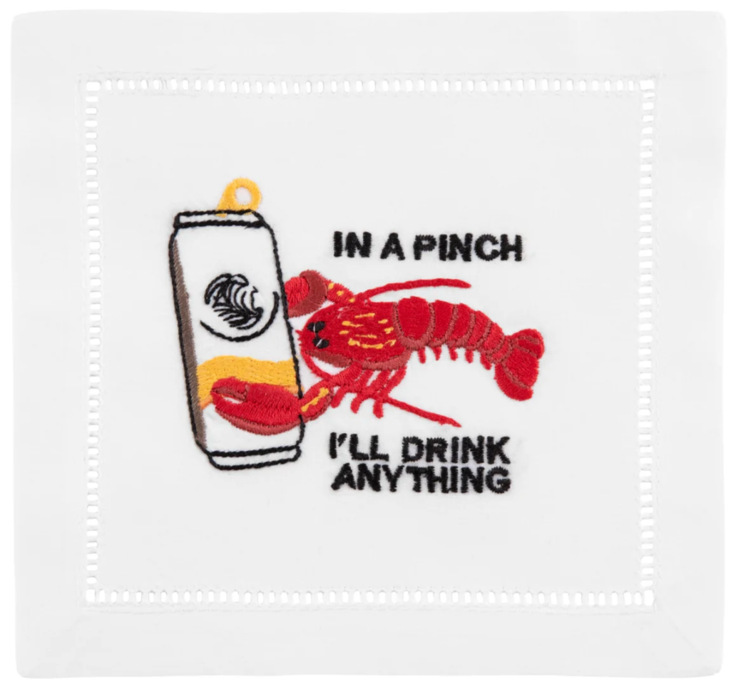 The August Morgan Lobster Cocktail Napkins feature classic hemstitching, an embroidered red lobster holding a can, and the phrase “IN A PINCH I’LL DRINK ANYTHING”—a playful touch for your next gathering.
