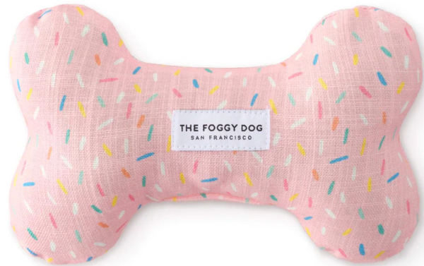 A pink, eco-friendly Foggy Dog Dog Bone Squeaky Toy with colorful sprinkles and a label that reads "the foggy dog San Francisco.