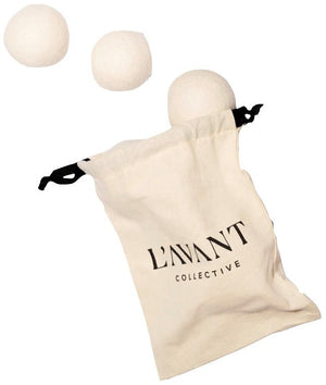 A beige drawstring bag labeled "L'Avant Collective" holds three eco-friendly Wool Dryer Balls by L'Avant Collective, made from New Zealand wool; two are outside the bag while one is partially tucked inside.