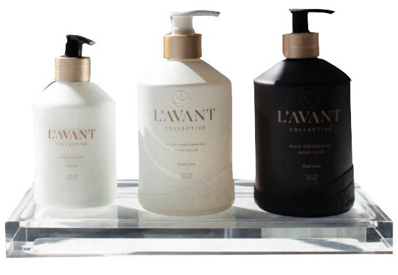 Two white and one black L’Avant Collective pump bottles are displayed on a Lucite Tray Large, highlighting a refined minimalist design against a white background.