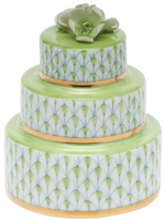 The Herend Wedding Cake is a three-tiered decorative box with green and gold accents, white patterned sides featuring hand-painted designs, and a green ceramic flower on top.