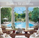 A lush outdoor seating area by a pool exudes Caribbean retreat vibes under a bright sky. The cover of "House by the Sea" by Abrams highlights its exquisite interior design.