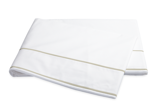 Two white folded Matouk Ansonia Bedding Collection Egyptian cotton percale bed sheets with a beige trim, isolated on a black background.