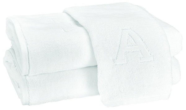 A Matouk Auberge Monogram Bath Towel with a monogrammed letter "a" stacked on top of it.
