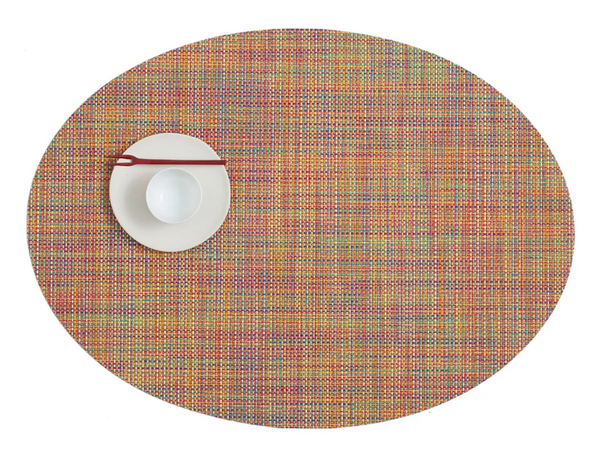 A white ceramic cup with a spoon inside sits on a saucer at the upper left side of an Oval Placemat, Confetti made from Terrastrand yarns by Chilewich.