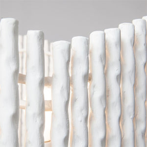 Close-up of the Camille Chandelier by Made Goods, featuring white cylindrical design with vertically aligned, twisted plaster bars and a partially visible light source behind them.