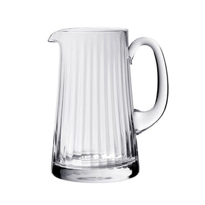 The William Yeoward Crystal Corinne Pitcher, a clear glass 2.5-pint vessel with vertical ridges, curved handle, and spout, features an elegant Jazz Age pattern and is displayed against a plain white background.