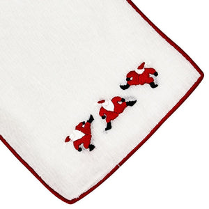 A set of four Haute Home 'Dancing Santa Coasters' featuring white linen with red trim, each adorned with hand-embroidered Santa figures in their classic red outfits and black boots.