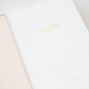 The Sugar Paper Tailored Chambray Journal is an open hardcover with a light pink cover, lined pages, gold "This journal belongs to" text on white paper.