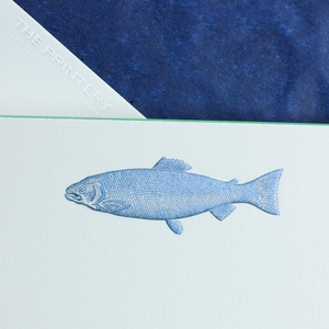 A small, detailed metallic blue fish is illustrated on textured white paper from the Fish Card Set by Printery, with a midnight blue envelope corner and "THE PRINTERY" in the top left.