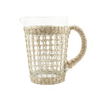 The Be Home Seagrass Cage Pitcher features clear glass wrapped with woven rattan and a matching handle, pictured on a white backdrop. This stylish seagrass pitcher adds natural charm to your table and is ideal for festive gatherings.