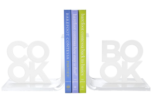 Three cookbooks by Ina Garten are displayed upright with Tara Wilson Designs' Cook Book Bookends, featuring sleek acrylic that spells "BOOK.